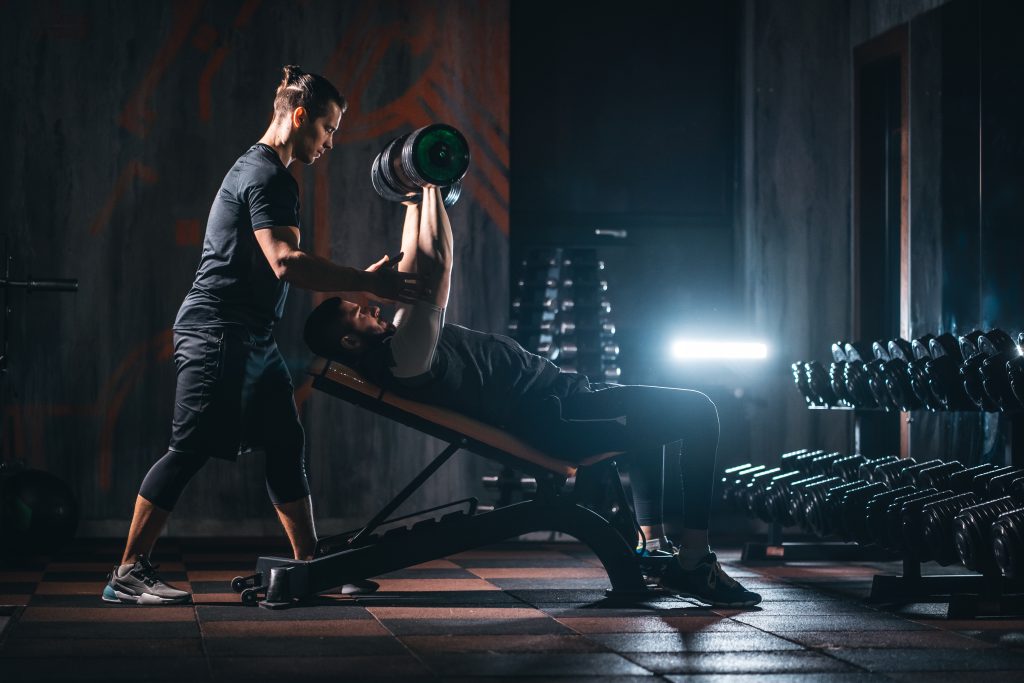 Young man has workout with personal trainer in modern gym