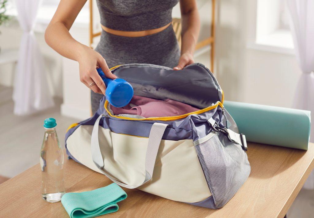 Packing gym bag essentials, sporty fit slim active beautiful young woman in sportswear, preparing